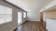 This single-floor unit is thoughtfully laid out, offering a comfortable and functional living environment. The open living area is a central highlight, featuring dark hardwood-style plank flooring that extends throughout the main living spaces, complemented by neutral gray walls and crisp white trim. Multiple windows fitted with horizontal blinds allow natural light to fill the room, creating a bright and welcoming atmosphere. Two entry doors provide convenient access points to the living area.

The kitchen is efficiently designed in a galley style, showcasing rich medium-toned wood cabinetry, granite-patterned countertops with a white tile backsplash, and black appliances including an electric range and dishwasher. A peninsula with a granite countertop and built-in sink opens toward the living space. Directly off the kitchen, a dedicated laundry closet houses a full-size washer and dryer.

The bedroom features soft carpeting, a ceiling fan with light fixture, and a window offering natural views. The bathrooms are consistently appointed with warm wood-framed mirrors, granite vanity countertops, rich cherry-toned cabinetry, and a tub-shower combination, providing a cohesive and polished finish throughout.