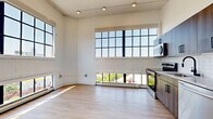 This thoughtfully designed single-floor unit blends industrial character with contemporary finishes throughout its five rooms. Soaring ceilings with exposed beams and ductwork lend an airy loft-like quality, while large factory-style multi-pane windows flood every room with abundant natural light and frame impressive city skyline views. Light-toned hardwood flooring runs continuously through the living areas and bedrooms, creating a warm, cohesive aesthetic.

The open-concept kitchen and living area serves as the heart of the unit, anchored by a full suite of stainless steel appliances, including a refrigerator, range, microwave, and dishwasher. Sleek wood-toned cabinetry with matte black hardware and a subway tile backsplash complete the modern kitchen aesthetic.

The bedrooms are bright and well-proportioned, each featuring high ceilings, large windows with city views, and ample double-door closet storage with matching black hardware. A hallway connects the rooms with clean white walls and recessed lighting.

The bathroom is finished to a high standard, offering a wood-grain vanity with a white quartz countertop, a matte black faucet, and a frameless glass walk-in shower with white subway tile surround and a linear drain. The overall ambiance throughout is clean, modern, and bright, with a nod to the building's industrial heritage.