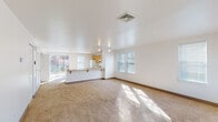 This two-story space offers a clean, functional layout designed for comfortable everyday living. The main level centers around a generously sized, open-plan living and dining area finished with wall-to-wall carpeting that carries natural light streaming in through multiple windows fitted with blinds. A front entry door with a transom window panel provides a welcoming introduction to the space. The kitchen is seamlessly integrated into the main living area via a peninsula counter with a breakfast bar overhang, offering casual seating and an open sight line. The kitchen itself is equipped with warm oak cabinetry, ample upper and lower storage, tile flooring, a full-size refrigerator, electric range with overhead ventilation, and a dishwasher. A full bathroom on this level features white square tile surrounds, a tub-shower combination, and tile flooring. The upper floor houses the bedrooms, each carpeted and filled with natural light from multiple windows. One bedroom includes a closet with bifold doors. A second full bathroom upstairs mirrors the clean, white-tiled design of the first. Throughout both floors, the neutral color palette and bright white walls create a light, airy ambiance.