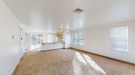 This two-story space offers a clean, functional layout designed for comfortable everyday living. The main level centers around a generously sized, open-plan living and dining area finished with wall-to-wall carpeting that carries natural light streaming in through multiple windows fitted with blinds. A front entry door with a transom window panel provides a welcoming introduction to the space. The kitchen is seamlessly integrated into the main living area via a peninsula counter with a breakfast bar overhang, offering casual seating and an open sight line. The kitchen itself is equipped with warm oak cabinetry, ample upper and lower storage, tile flooring, a full-size refrigerator, electric range with overhead ventilation, and a dishwasher. A full bathroom on this level features white square tile surrounds, a tub-shower combination, and tile flooring. The upper floor houses the bedrooms, each carpeted and filled with natural light from multiple windows. One bedroom includes a closet with bifold doors. A second full bathroom upstairs mirrors the clean, white-tiled design of the first. Throughout both floors, the neutral color palette and bright white walls create a light, airy ambiance.