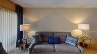 This single-floor residence offers a thoughtfully arranged layout that balances comfort and practicality across its key living areas. The living room serves as the heart of the home, featuring warm neutral walls, soft carpeted flooring, and a ceiling fan with a light fixture overhead. A large sliding glass door with vertical blinds allows natural light to fill the space, complemented by stylish floor lamps and a glass-topped coffee table that add a modern touch to the relaxed setting. A decorative chair rail runs along the walls, lending the room a subtle architectural detail.

The galley-style kitchen is efficiently designed with white cabinetry, dark granite-look countertops, and hardwood flooring. It is equipped with a full-size refrigerator, electric range, microwave, and a double stainless steel sink. A louvered bifold closet door provides convenient pantry or utility storage, and a skylight panel brightens the workspace.

The bedroom is spacious and serene, featuring plush carpeting, a ceiling fan, and a window dressed with sheer curtains that invite gentle natural light. The room offers ample space for a full furniture arrangement.

The bathroom is appointed with a dark granite-look vanity, wood flooring, and a shower-tub combination, completing this comfortable and move-in-ready residence.