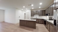 This single-floor residence showcases a thoughtfully designed, contemporary interior with a cohesive neutral color palette throughout. The kitchen serves as a focal point, featuring dark espresso cabinetry with ample upper and lower storage, light granite countertops with subtle veining, and a classic white subway tile backsplash. A substantial center island with matching granite provides additional workspace and casual seating. Stainless steel appliances, including a refrigerator with ice maker, electric range, built-in microwave, and dishwasher, complete the well-appointed kitchen. Recessed lighting illuminates the space effectively.

The open living area is finished with light wood-look flooring and features a ceiling fan and large sliding glass door that invites natural light. A hallway connects the main living spaces to the private areas of the home. Bedrooms are carpeted for comfort, each equipped with ceiling fans, windows for natural light, and built-in closets with shelving systems. The primary bedroom includes access to a walk-in closet with an organizational shelving unit.

Bathrooms are finished with wood-look tile flooring, dark vanity cabinetry, granite countertops, and tiled tub-shower combinations, maintaining the consistent, modern aesthetic found throughout the residence.