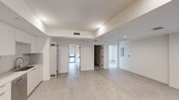 This thoughtfully designed single-floor unit offers a clean, contemporary aesthetic throughout its well-organized layout. The open-concept living and kitchen area serves as the heart of the space, featuring polished concrete-style flooring and recessed lighting that creates a bright, airy ambiance. The kitchen is outfitted with a full suite of stainless steel appliances — including a gas range, over-the-range microwave, dishwasher, and refrigerator — complemented by sleek, light wood-toned cabinetry, white upper cabinets, and a minimalist countertop with an integrated sink.

The bedroom is a serene, carpeted retreat bathed in natural light from a large black-framed sliding glass door that opens to a private balcony. Floor-length white curtains on a black double rod add an elegant touch. Built-in light wood cabinetry provides generous storage directly within the room.

The bathroom is efficiently designed with a light wood vanity, modern fixtures, and a spacious walk-in shower enclosed by black-framed glass doors and finished with grey tile surround and built-in niches. Small-format white mosaic tile floors complete the polished look.

Throughout the unit, crisp white walls, recessed lighting, and black-framed windows and doors create a cohesive modern design language.