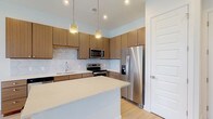 Located at 1341 Norton Ave in Columbus, Ohio's Grandview Heights area, this single-floor unit showcases a clean, contemporary design throughout. The open-concept kitchen is a standout feature, outfitted with warm wood-grain cabinetry that extends to the ceiling for ample storage, light quartz countertops, and a full suite of stainless steel appliances including a French door refrigerator, electric range, built-in microwave, and dishwasher. A tasteful subway tile backsplash adds texture, while pendant lighting illuminates the central island, creating an inviting space for cooking and entertaining. Light-toned hardwood-style flooring runs seamlessly throughout the main living areas, enhancing the bright and airy atmosphere. The living area is bathed in natural light and opens through a set of elegant French doors, offering outdoor access and views. The bathroom is finished with crisp white tile in a walk-in glass-enclosed shower, complemented by chrome fixtures for a polished look. A dedicated utility closet houses the water heater and HVAC system, keeping mechanical components neatly contained. The overall aesthetic is modern and move-in ready, with neutral tones and quality finishes throughout.