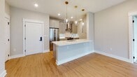 This well-designed single-floor residence offers a thoughtfully curated layout that balances modern aesthetics with everyday functionality. The heart of the home is an open-concept kitchen, highlighted by a large central island with a white quartz countertop and an integrated sink. Soft gray shaker-style cabinetry pairs elegantly with stainless steel appliances, including a French door refrigerator and a gas range beneath a wall-mounted hood. Three globe pendant lights suspended from brass fixtures add a warm, contemporary touch overhead, while light bamboo hardwood flooring extends throughout the main living areas. The spacious living area provides a clean, open canvas filled with recessed lighting, and a dedicated laundry alcove with a full-size washer and dryer is conveniently accessible from this space. The bedrooms are generously sized, each featuring neutral-toned walls, plush wall-to-wall carpeting, and windows dressed with horizontal blinds that allow ample natural light. Two bathrooms serve the residence, each finished with large-format tile flooring and surround, dark espresso-toned vanity cabinetry, white quartz countertops, and chrome fixtures. One bathroom features a full soaking tub with a curved shower rod, while the second offers a single vanity with a bright window. The overall ambiance is clean, modern, and move-in ready.