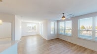 This well-appointed single-floor residence offers a clean, modern aesthetic throughout its thoughtfully designed layout. The open living and dining area is filled with natural light streaming through multiple windows fitted with horizontal blinds, complemented by light-toned hardwood-style flooring and a ceiling fan that enhances the airy ambiance. Views of the surrounding neighborhood are visible from multiple angles, adding to the sense of connection with the outdoors.

The kitchen is sleek and functional, featuring dark gray cabinetry, stainless steel appliances including a refrigerator, range, and microwave, a white quartz countertop, and a kitchen island with an undermount sink. Pendant lighting adds a contemporary finishing touch above the island.

The bedrooms are carpeted for comfort and each includes a ceiling fan and windows that allow in natural light. The primary bedroom connects directly to a well-designed bathroom featuring dark wood-toned cabinetry, a white countertop vanity, a large mirror with modern lighting, and hexagonal tile flooring. A walk-in closet with wire shelving is accessible from the bathroom, providing generous storage.

A dedicated in-unit laundry area houses a full-sized washer and dryer with overhead wire shelving, adding everyday convenience to this move-in ready residence.