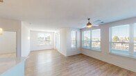 This well-appointed single-floor residence offers a clean, modern aesthetic throughout its thoughtfully designed layout. The open living and dining area is filled with natural light streaming through multiple windows fitted with horizontal blinds, complemented by light-toned hardwood-style flooring and a ceiling fan that enhances the airy ambiance. Views of the surrounding neighborhood are visible from multiple angles, adding to the sense of connection with the outdoors.

The kitchen is sleek and functional, featuring dark gray cabinetry, stainless steel appliances including a refrigerator, range, and microwave, a white quartz countertop, and a kitchen island with an undermount sink. Pendant lighting adds a contemporary finishing touch above the island.

The bedrooms are carpeted for comfort and each includes a ceiling fan and windows that allow in natural light. The primary bedroom connects directly to a well-designed bathroom featuring dark wood-toned cabinetry, a white countertop vanity, a large mirror with modern lighting, and hexagonal tile flooring. A walk-in closet with wire shelving is accessible from the bathroom, providing generous storage.

A dedicated in-unit laundry area houses a full-sized washer and dryer with overhead wire shelving, adding everyday convenience to this move-in ready residence.