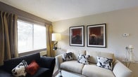 Located at 3970 Brelsford Lane in Dublin, Ohio, this single-floor residence offers a thoughtfully arranged living environment with a warm and inviting atmosphere. The living area serves as a central gathering space, featuring a neutral color palette that lends a calm, sophisticated ambiance. A large window dressed with elegant gold curtains and horizontal blinds allows abundant natural light to fill the room, creating a bright and airy feel. The space is furnished with a plush, light-toned sofa accented by bold black-and-white patterned throw pillows, complemented by a sleek dark accent chair with a rich red cushion. A stylish table lamp adds a soft warm glow, enhancing the cozy atmosphere. Two framed art prints displayed prominently on the wall add a refined, gallery-like quality to the room. The textured ceiling adds a classic architectural detail throughout. The overall design blends comfort with a polished aesthetic, making the living space both functional and visually appealing. Situated in the desirable Dublin, OH community, this residence offers convenient access to local amenities, dining, and recreation in one of Central Ohio's most sought-after neighborhoods.