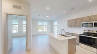 Located in Spring Lake, Michigan, this well-designed one-bedroom, one-bathroom unit offers a clean, modern aesthetic throughout. The open-concept kitchen and living area serves as the heart of the space, featuring a central island with a white quartz countertop and built-in sink, warm-toned flat-panel cabinetry, white subway tile backsplash, and a full suite of stainless steel appliances including a refrigerator, range, microwave, and dishwasher. Light hardwood flooring runs seamlessly across the entire unit, complementing the crisp white walls and creating a bright, cohesive atmosphere. Recessed lighting in the kitchen adds a polished touch. The living area is open and versatile, providing ample room for various furniture arrangements. The bedroom is comfortably sized, filled with natural light through large windows fitted with horizontal blinds that offer views of the surrounding neighborhood. The bathroom features a tub-shower combination, a floating wood vanity with a white countertop, and brushed nickel fixtures and grab bar accents. Throughout the unit, the design prioritizes simplicity and functionality, resulting in a fresh, contemporary living environment.