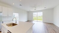 This two-story home features a clean, modern design characterized by white walls, light hardwood flooring throughout, and an abundance of natural light. The main floor hosts the primary living areas, including an open-concept kitchen and living room. The kitchen is equipped with white shaker-style cabinetry, a white quartz island with an undermount sink, stainless steel appliances including a refrigerator, range, and microwave, complemented by a white subway tile backsplash. The living area extends naturally from the kitchen, featuring a ceiling fan and large sliding glass doors that open to outdoor green views, flooding the space with natural light. A half bathroom with a pedestal sink is also located on the main floor. The staircase, featuring white balusters and warm wood treads, leads to the upper level, where four bedrooms are situated along a bright hallway. Each bedroom offers hardwood flooring and windows with outdoor views. The bathrooms on the upper floor include a full tub-shower combination with floor-to-ceiling neutral tile surround. A dedicated laundry room and closet complete the upper level, making this home both functional and well-organized throughout.
