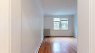 This single-floor unit blends classic architectural details with functional living spaces. The main living area is a highlight of the space, featuring warm hardwood floors that catch the natural light streaming in through large double-pane windows. Crown molding runs along the ceiling perimeter, adding a refined character to the room. A traditional cast-iron radiator provides efficient, even heating throughout the colder months.

Additional rooms continue the hardwood flooring and clean white walls, offering versatile spaces suited for a variety of uses. Each room benefits from natural light, with windows framing views of the surrounding neighborhood's mature trees. A paneled interior door with brass hardware adds a classic touch.

The kitchen is efficiently designed with white cabinetry, butcher block countertops, a white gas range, dishwasher, and full-size refrigerator, all set against a neutral-toned luxury vinyl plank floor. The layout maximizes the available space while maintaining a clean, cohesive aesthetic.

The bathroom is finished in white tile and features a soaking tub, a wall-mounted flush valve toilet, and a window that allows for natural ventilation. Wood-tone flooring completes the space, creating a warm contrast to the white tile surround. Overall, the unit presents a consistent, well-maintained character throughout.