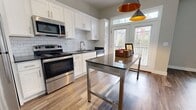 This contemporary apartment showcases a thoughtfully designed open-concept layout, maximizing space and natural light. The kitchen is a standout feature, boasting crisp white cabinetry, stainless steel appliances, and a stylish subway tile backsplash. A central island with a metallic finish provides additional counter space and casual seating.

The bathroom exudes elegance with its marble-look tile, glass shower enclosure, and modern vanity topped with a dark countertep. Wood-look flooring flows throughout the main living areas, while plush carpeting adds comfort to the bedrooms. Large windows in the living room and bedrooms flood the space with natural light, creating an airy ambiance.

The apartment's neutral color palette, predominantly whites and light grays, contributes to a clean and spacious feel. Distinctive lighting fixtures, including track lighting in the kitchen and a ceiling fan in the bedroom, add both functionality and style. The overall design emphasizes a harmonious blend of comfort and contemporary aesthetics, perfect for modern urban living.