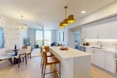 Located at 1602 S Federal Hwy in Boynton Beach, FL, this well-appointed 3-bedroom, 3-bathroom residence offers a thoughtfully designed open-concept layout across a single floor. Light wood-look flooring flows throughout the main living areas, lending a warm, contemporary feel. The kitchen serves as the heart of the home, showcasing crisp white cabinetry with gold hardware, a striking marble-veined waterfall island, stainless steel appliances, and a suite of bold gold pendant lights that add a luxurious touch. The kitchen opens seamlessly into the living room, which is brightened by a ceiling fan and large sliding glass doors leading to a private balcony with outdoor views. Each of the three bedrooms features plush carpeting, generous closet space with built-in shelving, and sliding glass doors that connect to the balcony, filling the rooms with natural light. The three bathrooms are finished in neutral tones with marble-style tile surrounds and soaking tub-shower combinations. A dedicated in-unit laundry area houses a full-size washer and dryer. The overall ambiance is clean, modern, and move-in ready, reflecting a cohesive design palette of whites, neutrals, and gold accents throughout.