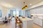 Located at 1602 S Federal Hwy in Boynton Beach, FL, this well-appointed 3-bedroom, 3-bathroom residence offers a thoughtfully designed open-concept layout across a single floor. Light wood-look flooring flows throughout the main living areas, lending a warm, contemporary feel. The kitchen serves as the heart of the home, showcasing crisp white cabinetry with gold hardware, a striking marble-veined waterfall island, stainless steel appliances, and a suite of bold gold pendant lights that add a luxurious touch. The kitchen opens seamlessly into the living room, which is brightened by a ceiling fan and large sliding glass doors leading to a private balcony with outdoor views. Each of the three bedrooms features plush carpeting, generous closet space with built-in shelving, and sliding glass doors that connect to the balcony, filling the rooms with natural light. The three bathrooms are finished in neutral tones with marble-style tile surrounds and soaking tub-shower combinations. A dedicated in-unit laundry area houses a full-size washer and dryer. The overall ambiance is clean, modern, and move-in ready, reflecting a cohesive design palette of whites, neutrals, and gold accents throughout.