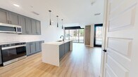 Located at 855 N. Broadway in Denver, CO, this modern two-story condo spans 1,360 square feet across two floors, offering 3 bedrooms and 3 bathrooms. The ground floor (590 sq ft) features an open-concept kitchen and living area bathed in natural light through expansive floor-to-ceiling sliding glass doors that frame urban views of the Broadway corridor. The kitchen is appointed with two-tone shaker cabinetry in gray and blue, white quartz countertops, stainless steel appliances, a large island with an undermount sink, and stylish pendant lighting. Light hardwood flooring flows throughout both levels, complemented by a concrete accent column that adds an industrial touch. The upper floor (770 sq ft) houses all three bedrooms, including a 270-square-foot primary suite with an en-suite bathroom featuring a glass-enclosed shower, gray shaker vanity with white quartz countertops, matte black hardware, large-format tile flooring, and a dedicated walk-in closet. Secondary bathrooms mirror the same refined aesthetic with full tub-shower combos and coordinating finishes. A staircase connects both floors, and the layout also includes a hallway and additional closet space for practical storage.