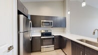 Located at 11901 S Freedom Park Dr in Herriman, Utah, this thoughtfully designed single-floor residence combines modern finishes with a clean, functional layout. The kitchen serves as a standout feature, showcasing dark espresso-toned cabinetry with sleek hardware, white quartz countertops, and a full suite of stainless steel appliances including a refrigerator, range, microwave, and dishwasher. A peninsula with an undermount sink and pendant lighting above adds both style and practicality, creating an ideal space for cooking and casual dining. Light wood-style flooring runs through the kitchen and main living areas, lending warmth and continuity throughout. The living space is open and airy with neutral warm-toned walls and ample natural light flowing in through sizable windows dressed with horizontal blinds. The bedrooms feature plush carpeting, generous wall space, and windows that offer views of the surrounding neighborhood. Closet access is conveniently integrated into the bedroom layout. The bathroom is finished with large-format tile flooring, white cabinetry with a dark countertop, a well-lit vanity mirror, and a full tub and shower combination. The overall design palette is cohesive, contemporary, and move-in ready.