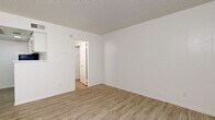 Located at 3708 W Camelback Rd in Phoenix, Arizona, this single-floor unit offers a efficiently designed layout comprising a living room and a full bathroom. Light wood-look luxury vinyl flooring runs throughout the entire space, lending warmth and visual continuity to every room. The living area is bright and open, featuring crisp white walls, a textured ceiling, and a window fitted with vertical blinds that allows natural light to filter in. A front entry door opens directly into this main living space, keeping the layout simple and accessible. A compact kitchen area is defined by a white pass-through counter and overhead cabinetry, seamlessly connecting to the living space while maximizing the use of available square footage. Ceiling vents indicate a central HVAC system for year-round comfort. The bathroom is neatly appointed with a white vanity featuring under-sink storage, a wall-mounted medicine cabinet with mirror, and a walk-in shower, all finished in a clean, neutral palette. The consistent use of white throughout the walls, trim, and fixtures creates a cohesive, well-lit environment. Overall, this unit presents a functional and tidy space suited for efficient everyday living in the heart of Phoenix.