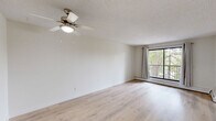 Located at 360 Falshire Dr NE in Calgary's northeast, this well-laid-out two-bedroom, two-bathroom unit offers a comfortable and functional living space across a single floor. The interior has been updated with light hardwood flooring throughout, creating a bright and cohesive aesthetic that flows from room to room.

The open living area is generously proportioned, featuring a ceiling fan and access to a balcony framed by large windows dressed with neutral drapes, offering pleasant views of mature trees. The space connects seamlessly toward the kitchen area, which is visible in the background with its light cabinetry.

Both bedrooms are well-sized, each benefiting from natural light through windows that overlook greenery. The primary bedroom is notably spacious, with a textured ceiling and baseboard heating. Each bedroom is fitted with folding-door closets in a dark finish, providing practical storage. Light hardwood flooring continues throughout both rooms.

The two bathrooms are identically appointed, each featuring a single-sink vanity with warm wood cabinetry, a large mirror with overhead lighting, and a full tub-shower combo with white tile surround. A dedicated closet adds additional storage to the unit. The overall palette of whites and light neutrals gives the space a clean, airy character.