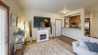 This thoughtfully designed 2-bedroom, 2-bathroom single-floor residence offers a comfortable and functional layout across a well-utilized footprint. The open-concept living, dining, and kitchen area serves as the heart of the home. The living room features plush carpeting, a wall-mounted TV above a white electric fireplace, a wall-mounted mini-split unit, and large windows with blinds that invite natural light and provide outdoor views. A private door leads directly outside from the living area. The adjacent dining space accommodates a round table for four and features hardwood-style flooring that continues into the kitchen. The kitchen is equipped with warm wood cabinetry, stainless steel appliances including a refrigerator, range, and microwave, a double sink, and a pass-through counter connecting to the living area. The primary bedroom offers generous proportions, dual windows with views of greenery, carpeted flooring, and direct access to both a closet and a private bathroom. The second bedroom is similarly comfortable with its own closet and access to the second full bathroom. Both bathrooms feature a tub-shower combination, tile flooring, and wood-toned vanity cabinetry. A dedicated closet provides additional storage, rounding out this practical and inviting home.