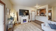 This thoughtfully designed 2-bedroom, 2-bathroom single-floor residence offers a comfortable and functional layout across a well-utilized footprint. The open-concept living, dining, and kitchen area serves as the heart of the home. The living room features plush carpeting, a wall-mounted TV above a white electric fireplace, a wall-mounted mini-split unit, and large windows with blinds that invite natural light and provide outdoor views. A private door leads directly outside from the living area. The adjacent dining space accommodates a round table for four and features hardwood-style flooring that continues into the kitchen. The kitchen is equipped with warm wood cabinetry, stainless steel appliances including a refrigerator, range, and microwave, a double sink, and a pass-through counter connecting to the living area. The primary bedroom offers generous proportions, dual windows with views of greenery, carpeted flooring, and direct access to both a closet and a private bathroom. The second bedroom is similarly comfortable with its own closet and access to the second full bathroom. Both bathrooms feature a tub-shower combination, tile flooring, and wood-toned vanity cabinetry. A dedicated closet provides additional storage, rounding out this practical and inviting home.