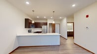 Located at 9941 S 37th St in Lincoln, Nebraska, this thoughtfully designed one-bedroom, one-bathroom unit offers a functional and modern single-floor layout. The open-concept living and kitchen area forms the heart of the space, where light-toned walls and recessed lighting create a bright, welcoming atmosphere. The kitchen is a standout feature, boasting rich dark espresso cabinetry, crisp white countertops, and a full suite of stainless steel appliances including a refrigerator, range, microwave, and dishwasher. A peninsula with pendant lighting serves as a natural divider between the kitchen and the carpeted living area, which is anchored by a private entry door and a large window with vertical blinds that invites natural light. The bedroom offers a comfortable, carpeted retreat complete with a ceiling fan and a generous window. A spacious walk-in closet with multi-level shelving and hanging rods provides ample storage. The full bathroom is finished with dark wood cabinetry, a white countertop vanity, a large mirror, and a tub-shower combination, all set on light wood-look flooring that ties the space together cohesively.