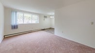 This single-floor 1-bedroom, 1-bathroom unit at Hazelwood in Inkster, Michigan presents a clean, well-organized layout designed for comfortable everyday living. The living area features soft wall-to-wall carpeting underfoot and a large picture window that fills the space with natural light and provides views of the surrounding greenery. A wall-mounted air conditioning unit and baseboard heating ensure year-round climate comfort. Adjacent to the living area, a defined dining space is accented by a classic chandelier and durable wood-look flooring that continues into the kitchen. The galley-style kitchen is efficiently arranged with rich dark wood cabinetry lining both sides, white countertops, a built-in sink, and white appliances including a coil-burner range and refrigerator, providing ample storage and prep space. The bedroom is a generously sized, quiet retreat with plush carpeting, a wide window overlooking outdoor scenery, and baseboard heating. A spacious walk-in closet off the bedroom offers dual shelving on both sides, providing substantial storage capacity. The full bathroom features classic white tile surrounding a full soaking tub and shower, a pedestal-style vanity with a mirror cabinet, and mosaic tile flooring, delivering a clean and functional design throughout.