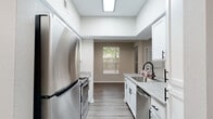 This single-story home offers a thoughtfully designed layout with a clean, modern aesthetic throughout. The galley-style kitchen is a standout feature, equipped with stainless steel appliances including a refrigerator, range, microwave, and dishwasher. Crisp white cabinetry with matte black hardware pairs with light stone-look countertops, while wood-look luxury vinyl flooring and a skylight-style overhead fixture keep the space bright and functional. A window at the end of the kitchen allows natural light to flow through.

The bedrooms feature plush carpeting, neutral-toned walls, and windows with blinds that bring in natural light. Ceiling fans are present in select bedrooms, adding comfort and airflow. Crown molding accents one of the bedroom spaces, lending a refined touch.

The bathrooms are well-finished, with one featuring a tub-shower combination surrounded by classic white tile with a decorative accent band, oil-rubbed bronze fixtures, and a vanity with a wood-toned countertop. A second bathroom includes a spacious layout with light vinyl flooring and a shower with a curtain enclosure.

A dedicated in-unit laundry area houses a full-size washer and dryer with overhead shelving. The overall palette of warm neutrals, black hardware accents, and consistent flooring materials creates a cohesive and move-in-ready living environment.