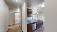 Located at 39 9th St in East Wenatchee, WA, this single-floor, 3-bedroom, 2-bathroom home offers a well-designed layout with comfortable living spaces throughout. The open-concept kitchen and living area serves as the heart of the home, showcasing rich dark wood cabinetry, granite countertops, stainless steel appliances including a range, microwave, refrigerator, and dishwasher, and stylish pendant lighting. The kitchen island with an integrated sink adds both functionality and visual appeal, while wood-style flooring anchors the space with warmth. The adjacent living room is generously sized, featuring plush carpet, neutral wall tones, and a glass door with a flanking window that invites natural light and outdoor views. A dedicated laundry room with a full-size washer and dryer adds everyday convenience. Each of the three bedrooms is finished with soft carpet and clean neutral walls, offering comfortable and versatile spaces. The primary bedroom is notably spacious. The two bathrooms are well-appointed, one featuring a full soaking tub with a shower surround and wood-style flooring. Throughout the home, the consistent use of neutral tones, dark trim accents, and quality finishes creates a cohesive and inviting atmosphere.