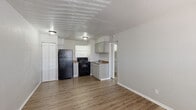 Located at 416 Sundown Dr in Independence, Missouri, this single-floor, one-bedroom, one-bathroom unit offers a practical and efficient layout across a compact footprint. The interior is finished with wood-look laminate flooring throughout, providing a cohesive and easy-to-maintain surface across all rooms.

The open living area serves as the central space of the unit, featuring neutral textured walls, a textured ceiling, and a window with horizontal blinds that allows natural light to filter in. A wall-mounted window air conditioning unit provides climate control. The entry door opens directly into this area, creating an accessible and straightforward flow.

The kitchen is positioned adjacent to the living space and features gray lower and upper cabinetry, a double-basin stainless steel sink with a window above it, a black electric range, and a black refrigerator. Counter space is functional, with a brown laminate surface running along the cabinetry.

The bedroom is a well-defined private space with neutral walls, laminate flooring, a window, and a six-panel door. A hallway connects the bedroom to the bathroom, which includes a full tub-shower combination with a curtain rod, a toilet, and built-in shelving, all finished in clean white tones.