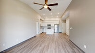 This single-story unit showcases a clean, modern design throughout, with light wood-look flooring in the main living areas and plush carpet in the bedrooms. The open-concept living and dining area is anchored by vaulted ceilings and a ceiling fan with integrated lighting, creating a bright and airy atmosphere. A sliding glass door leads to a private balcony, allowing natural light to fill the space while offering outdoor views.

The kitchen is well-appointed with white shaker-style cabinetry, light quartz countertops, a full suite of stainless steel appliances including a range, microwave, dishwasher, and refrigerator, and a central island that provides additional prep and dining space. Recessed lighting adds to the kitchen's bright, functional character.

The bedrooms feature plush carpeting and generous closet space, including a sliding-door closet with wire shelving. One bedroom offers direct access to a private bathroom, while a second full bathroom serves the remaining rooms. Both bathrooms include white vanity cabinetry, light countertops, and wood-look flooring. A dedicated laundry room houses a full-size washer and dryer alongside wire shelving for additional storage.