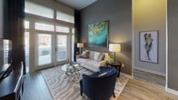 This single-floor residence showcases a modern, open-concept design with impressive soaring ceilings that enhance the sense of space throughout. The living area is anchored by large floor-to-ceiling windows and a glass-paneled door that floods the room with natural light, complemented by wood-look flooring and a neutral color palette accented with bold artwork.

The kitchen is a standout feature, boasting dark cabinetry, stainless steel appliances, a subway tile backsplash, and a granite-topped island with pendant lighting — ideal for both cooking and casual dining, with bar seating provided by teal upholstered chairs.

The bedrooms offer distinct personalities: one features a bold green accent wall paired with a wood-framed bed and walk-in closet access, while another presents a sophisticated gray palette with coordinating navy and teal accents. Each bedroom benefits from ample natural light through large windows with decorative drapery.

The bathrooms are finished with granite vanity tops, dark cabinetry, and tile flooring. One bathroom provides direct access to a walk-in closet, adding practical functionality. Throughout the space, consistent use of teal, navy, and green tones creates a cohesive and polished aesthetic that ties each room together seamlessly.