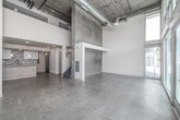 Located in the heart of Los Angeles' vibrant Arts District at 950 E 3rd St, this two-floor loft delivers an industrial-modern aesthetic across a well-apportioned layout. The main level impresses immediately with soaring double-height ceilings, polished concrete floors, and raw exposed concrete walls that lend an authentic urban character. Floor-to-ceiling windows and glass sliding doors flood the living area with abundant natural light and open directly onto a landscaped outdoor patio, offering seamless indoor-outdoor living with views of the surrounding neighborhood. The kitchen is thoughtfully designed, featuring wood-toned cabinetry with gold hardware, a hexagonal tile backsplash, stainless steel appliances including a French door refrigerator and dishwasher, and a central island with pendant lighting overhead. Two full bathrooms serve the residence — one with a soaking tub and classic subway tile surround, and another with a glass-enclosed walk-in shower finished in white subway tile. An upper loft level provides additional flexible living space, accessible via a staircase. Three closets, a dedicated laundry area, and a hallway round out the functional amenities of this architecturally distinctive urban loft.