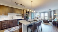 This single-floor residence offers a thoughtfully designed open-concept layout that seamlessly connects the kitchen, dining, and living areas. The kitchen is a standout feature, showcasing rich walnut-toned cabinetry, a white quartz countertop island with bar seating, stainless steel appliances, a tile backsplash, and both track and pendant lighting. The island serves as a natural transition into the dining and living spaces.

The living room is bright and inviting, featuring wood-look flooring, a soft accent wall in a calming aqua tone, and large windows with outdoor access that bring in generous natural light. The space accommodates comfortable seating arrangements and stylish décor.

Two bedrooms provide restful retreats, each with plush carpeting and distinct accent walls — one in aqua and another in soft lavender — creating a warm, personalized atmosphere. Both rooms benefit from ample natural light through large windows with ceiling fans or thoughtful lighting fixtures.

Two bathrooms feature warm wood vanities with white countertops, well-lit mirrors, and a combination of soaking tubs and glass-enclosed showers. One bathroom includes direct access to a walk-in closet. Wood-look flooring carries throughout the bathrooms, maintaining a cohesive aesthetic across the entire residence.