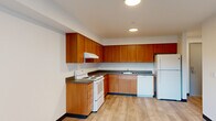 This 2-bedroom, 1-bathroom residence is thoughtfully laid out across a single floor, offering a practical and clean living environment. The kitchen is a standout feature, showcasing warm honey-toned wood cabinetry that extends along two walls in an L-shaped configuration, providing generous storage space. Dark countertops offer a pleasant contrast to the cabinetry, while white appliances — including an electric range, dishwasher, and refrigerator — complete the functional setup. Recessed ceiling lighting illuminates the kitchen, which flows openly into the main living area. Light hardwood-style flooring runs consistently throughout the space, adding warmth and cohesion to every room. The primary bedroom is a comfortable size and features two sliding-door closets, a ceiling fan with light fixture, and a window that invites natural light. The second bedroom also benefits from a window with outdoor views and a ceiling fan. A hallway connects the bedrooms and living areas to the full bathroom, which is fitted with a tub-shower combination, a vanity with wood cabinetry, and speckled tile flooring. The overall design is clean and straightforward, with neutral white walls and dark baseboards providing a simple, functional aesthetic throughout.