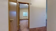 Located at 803 S Cowley St in Spokane, WA, this single-floor unit offers a thoughtfully arranged layout with notable architectural details throughout. The living room serves as the centerpiece of the space, featuring soaring vaulted ceilings that create an open, airy atmosphere. A tile-surround fireplace with a classic wood mantel anchors the room, while corner windows allow abundant natural light and outdoor views to fill the space. Plush carpeting runs throughout the living areas and bedrooms, adding warmth underfoot.

The galley-style kitchen is efficiently designed with oak-trimmed cabinetry, white appliances including a range, dishwasher, and refrigerator, and durable tile flooring. A dedicated utility area just off the kitchen houses a stacked washer and dryer unit alongside a water heater, providing convenient in-unit laundry.

The bedroom features vaulted ceilings that mirror the living room, a baseboard heating unit, and a window with outdoor views. An adjoining walk-in closet offers built-in wood shelving and hanging rods for ample storage. The bathroom includes a vanity with oak-accented cabinetry, tile flooring, and a separate water closet, combining practicality with a clean, neutral aesthetic throughout.