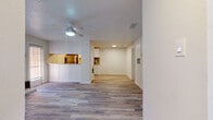 This single-floor residence presents a thoughtfully designed layout that balances open living areas with functional private spaces. Throughout the home, light-toned wood-look flooring creates a cohesive and modern aesthetic, complemented by neutral white walls and textured popcorn ceilings.

The living room is a welcoming central space, anchored by a classic white-surround fireplace and a ceiling fan overhead. Natural light filters in through slatted blinds, brightening the room and highlighting its spacious feel. An adjacent dining or flex area extends the open-concept flow, connecting seamlessly to the kitchen via a pass-through window.

The kitchen is well-equipped with white cabinetry, granite-style countertops, stainless steel appliances including a refrigerator, electric range, and microwave, and a distinctive herringbone tile backsplash that adds a decorative touch. The galley-style layout maximizes efficiency.

The bedrooms are generously proportioned, each featuring ceiling fans and ample natural light from large windows. The bathroom includes a white vanity with an integrated countertop sink, offering clean and practical storage.

A hallway connects the private areas of the home, with convenient access to utility spaces. The overall ambiance is bright, clean, and move-in ready, making it a versatile and inviting space.