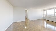This penthouse unit at 765 Steeles Ave W in Toronto offers a practical and well-organized layout across a single floor, comprising two bedrooms, two bathrooms, a combined kitchen and living room, and a dedicated closet. The living area is generously sized, featuring classic parquet wood flooring throughout and crisp white walls that create a bright, clean aesthetic. Large windows allow natural light to fill the space, with the primary bedroom offering elevated views over the surrounding treetops and cityscape. The kitchen is fitted with white cabinetry, dark countertops, and stainless steel appliances including a full-size refrigerator, stove, and dishwasher, with glossy tile flooring adding a polished finish. The primary bedroom is a well-proportioned retreat with parquet flooring and access to in-unit stacked laundry — a convenient feature tucked neatly within the space. The second bedroom also features parquet flooring and ample room. The two bathrooms are cleanly finished; one includes a soaker tub framed by neutral grey tile surround with chrome fixtures. Throughout, the unit maintains a consistent, neutral palette that provides a versatile and move-in-ready living environment.