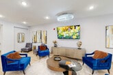 Located at 42280 Garfield Rd in Clinton Township, Michigan, this thoughtfully designed single-floor facility offers a generous and well-appointed layout across its expansive footprint. The space is organized to support both social gathering and everyday functionality.

The welcoming entrance lobby immediately sets an upscale tone, featuring light hardwood flooring, elegant crystal chandeliers, and stylish blue velvet accent chairs arranged around a circular glass coffee table. Vibrant abstract wall art and a wall-mounted flat-screen TV add visual interest, while a credenza with decorative accents completes the refined atmosphere.

The spacious dining room is a standout feature, accommodating multiple dining tables set with lantern centerpieces and neatly upholstered gray chairs with wood-tone legs. Tray ceilings with recessed lighting and a crystal chandelier lend architectural sophistication, while large windows dressed with warm-toned drapes invite natural light throughout.

A dedicated meeting room provides a more intimate setting, centered around a striking oval marble-top table surrounded by plush gray swivel chairs and equipped with a wall-mounted display screen — ideal for private discussions or presentations.

Connecting these areas is a bright, open hallway with light hardwood flooring, crystal overhead lighting, and a clean, modern aesthetic that ties the entire space together cohesively.