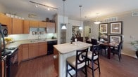 This single-story residence offers a thoughtfully designed layout that balances functionality with comfortable living. The living room serves as the central gathering space, featuring warm hardwood-style flooring, crown molding, a ceiling fan, and large sliding glass doors dressed with floor-length drapes that invite natural light and outdoor views. A cushioned sofa and accent chair anchor the room around a wood-framed glass coffee table, creating an inviting atmosphere.

The kitchen is well-equipped with warm wood cabinetry, black appliances including a refrigerator, range, microwave, and dishwasher, along with ample counter space and a double sink. A central island with pendant lighting and bar seating connects seamlessly to a dedicated dining area, making the space well-suited for both everyday meals and entertaining.

Both bedrooms are carpeted and include ceiling fans, generous windows with outdoor views, and ample closet space. Each is served by a full bathroom featuring a tub-shower combination with tile surround, wood-style flooring, and a vanity with storage.

A dedicated laundry area houses a full-sized washer and dryer with shelving above, adding everyday convenience to this well-rounded residence.