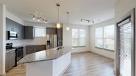 This well-appointed two-bedroom, two-bathroom single-story residence offers a thoughtfully designed open-concept layout with modern finishes throughout. The kitchen serves as a central focal point, showcasing dark wood-tone cabinetry, granite countertops, a classic white subway tile backsplash, and a full suite of stainless steel appliances including a gas range, microwave, and French door refrigerator. A curved kitchen island with an undermount sink and pendant lighting above provides additional workspace and casual seating, flowing naturally into the open living and dining area. Light wood-style plank flooring extends across the main living spaces, complemented by track lighting and multiple windows dressed with horizontal blinds that invite generous natural light.

Both bedrooms feature plush wall-to-wall carpeting and ceiling fans, with windows offering outdoor views. The primary bathroom is equipped with a double-sink vanity topped in granite, a soaking tub, and a tiled shower surround. The secondary bathroom mirrors the refined aesthetic with a granite-topped single vanity and tiled shower. Throughout the unit, a neutral color palette and consistent use of quality materials create a cohesive, contemporary ambiance.