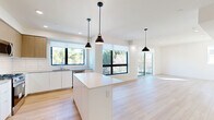 Located in Studio City, Los Angeles, this contemporary 3-bedroom, 2-bathroom home showcases a clean, modern aesthetic throughout. The open-concept living, dining, and kitchen area serves as the heart of the home, featuring light hardwood flooring, recessed lighting, and an abundance of natural light streaming through large black-framed windows and sliding glass doors. The kitchen is thoughtfully designed with white cabinetry, warm wood upper cabinets, a white quartz island, a subway tile backsplash, and stainless steel appliances, including a French door refrigerator and dishwasher. Stylish pendant lights hang above the island, adding a contemporary touch. The living area opens directly onto a private balcony with glass railings, offering views of palm trees and the surrounding neighborhood. The spacious primary bedroom features sliding glass doors to the balcony, large windows, and access to a generous walk-in closet with built-in shelving and hanging rods. Two additional bedrooms offer hardwood floors and ample closet space. The bathrooms are finished with marble-style tile flooring, white vanities, quartz countertops, and glass-enclosed showers. A dedicated laundry area and pantry add further functionality to this well-appointed home.