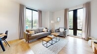 Located at 1 E Pleasant St in Amherst, MA, this apartment offers three bedrooms and two bathrooms across a single, efficiently designed floor. The living room is a standout space, bathed in natural light through large floor-to-ceiling windows with views of surrounding greenery. Light hardwood-style flooring runs throughout the main living areas, lending warmth and continuity to the open layout. The modern kitchen features sleek, handle-free white cabinetry extending to the ceiling, a clean white countertop, stainless steel appliances including a dishwasher, range, and over-the-range microwave, and direct access to natural light from a nearby window. The three bedrooms are carpeted for comfort, each featuring crisp white walls. The primary bedroom is a well-proportioned retreat with large windows and outdoor views, while the additional bedrooms offer cozy, functional spaces — one with a built-in closet with shelving. The two bathrooms are clean and contemporary: one features a glass-enclosed walk-in shower with white tile and wood-look flooring, while the second includes a full soaking tub and shower combination. A connecting hallway ties all rooms together in a practical and cohesive floor plan.