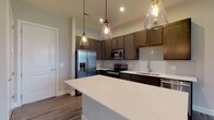 Located at 891 Ingleside Ave in Columbus, Ohio, this single-floor residence combines modern design with functional living. The open-concept kitchen serves as the heart of the space, showcasing rich dark-stained cabinetry, crisp white quartz countertops, and a full suite of stainless steel appliances including a French door refrigerator, electric range, built-in microwave, and dishwasher. A central island with pendant lighting provides additional prep space and a casual gathering spot, while a white subway tile backsplash adds a clean, contemporary touch. Wood-look plank flooring flows throughout the main living areas, lending warmth and visual continuity. The bedroom is finished with plush wall-to-wall carpeting and features a window that brings in natural light. The bathroom is appointed with a wide quartz vanity, dark-framed mirror, a walk-in glass-enclosed shower, and direct access to a spacious walk-in closet complete with built-in shelving and hanging storage. Throughout the unit, neutral wall tones and recessed lighting create a bright, inviting atmosphere that complements the cohesive, modern aesthetic of the overall design.