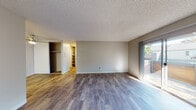 Located at 21701 Foothill Blvd in Hayward, California, this single-floor unit offers a well-organized layout with a variety of functional spaces throughout. The main living area is spacious and open, featuring rich, dark wood-style flooring and a textured ceiling that adds character. A sliding glass door floods the room with natural light and provides direct access to the outdoors, while vertical blinds offer privacy. Built-in shelving is conveniently accessible from the living area, providing ample storage. The kitchen is clean and modern, outfitted with white shaker-style cabinetry, gray countertops, a stainless steel dishwasher and refrigerator, and a range, all illuminated by a ceiling-mounted skylight panel. The bedroom features plush carpeting, a large window framing a view of surrounding greenery, a baseboard heater, and a textured ceiling. The bathroom is neatly appointed with white vanity cabinetry, gray countertops, a large mirror, and a shower-tub combination. An additional room with wood-style flooring and a baseboard heater connects to the kitchen area, enhanced by a ceiling fan. Throughout the unit, neutral tones and consistent finishes create a cohesive and comfortable ambiance.