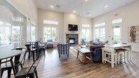 Located at 3001 Summit Dr in South Park, PA, this single-floor community space offers a well-appointed layout across three distinct areas designed for gathering and recreation. The open-concept kitchen and living room is a standout centerpiece, featuring soaring ceilings, recessed lighting, and rich hardwood-style flooring throughout. The kitchen is equipped with dark espresso cabinetry, a large white quartz island with bar seating for multiple guests, stainless steel appliances including a French door refrigerator, and ample counter space. The living room flows naturally from the kitchen and is anchored by a striking stacked-stone fireplace with a white mantle and a wall-mounted television above. Generous windows and transom lights flood the space with natural light, while views of an outdoor pool area add to the open, airy ambiance. The game room provides a lively recreational retreat, highlighted by a full-size pool table set beneath ample natural light from oversized windows, complemented by eclectic wall décor. The dining room offers an intimate setting with a round wooden table, leather chairs, a wall-mounted television, and large windows overlooking lush greenery. Consistent hardwood-style flooring and a neutral color palette unify the entire space.