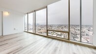 Located on a high floor at 3150 Wilshire Blvd in Los Angeles, this modern one-bedroom, one-bathroom residence offers a sleek, contemporary design throughout. Light wood-tone flooring runs consistently across the entire unit, complementing the clean white walls and creating a bright, cohesive aesthetic.

The open-concept living, dining, and kitchen area is the heart of the home, anchored by dramatic floor-to-ceiling windows that frame sweeping panoramic views of the Los Angeles skyline and cityscape. The kitchen is well-appointed with stainless steel appliances — including a gas range, dishwasher, microwave, and refrigerator — paired with dark lower cabinetry, crisp white upper cabinets, black granite countertops, and a tasteful mosaic tile backsplash. A dark-finished kitchen island provides additional prep and dining space.

The bedroom is a clean, minimalist retreat with the same light flooring and access to generous closet storage. Two closets provide ample organization throughout the unit, complemented by a full bathroom. Cylindrical surface-mounted light fixtures add a modern industrial touch to the ceilings. The overall ambiance is bright, airy, and contemporary, with the expansive city views serving as a defining architectural feature of this high-rise residence.