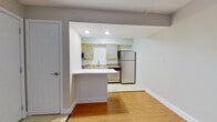 This single-floor unit presents a practical and well-organized layout with a neutral color palette and consistent finishes throughout. The kitchen is a standout feature, equipped with stainless steel appliances including a gas range, dishwasher, refrigerator, and microwave. Light wood cabinetry with frosted glass inserts, granite countertops, a subway tile backsplash, and recessed lighting give the kitchen a polished, modern feel. A peninsula counter connects the kitchen to the adjacent living area, creating an open and functional transition between spaces.

The living area is generously sized, featuring warm wood-style flooring and a decorative fireplace mantle that adds character to the room. A narrow window near the entry door allows natural light to filter in. A separate room with a large window overlooking greenery provides a bright and versatile space suitable for use as a bedroom or office.

The bathroom includes tile flooring, a full tub-shower combination with a clean white surround, and a granite-topped vanity with an undermount sink. Throughout the unit, clean white baseboards, neutral gray-toned walls, and consistent flooring create a cohesive and move-in ready environment.