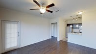 This single-floor residence in Frisco offers a clean, modern layout designed for comfortable everyday living. The open living area immediately draws attention with its rich, dark hardwood flooring that extends throughout, creating a warm and cohesive aesthetic. A classic ceiling fan with a built-in light fixture anchors the room, providing both comfort and illumination. Crisp white walls and white baseboards lend the space a bright, airy feel, while the open floor plan allows for flexible furniture arrangements to suit a variety of lifestyles. A doorway from the living area provides seamless access to additional rooms, enhancing the overall flow of the home. Adjacent to the living space, the kitchen is equipped with dark espresso cabinetry that offers generous storage, stainless steel appliances including a full-sized refrigerator, and a light-toned countertop that provides a striking contrast. Stylish pendant lighting hangs above the kitchen area, adding a touch of modern elegance. The transition between the kitchen and living area is smooth and intuitive, making the space well-suited for both daily routines and entertaining. Overall, this residence combines practical functionality with contemporary design details throughout.