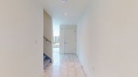 This modern two-story residence offers a generous 1410 square feet of living space, thoughtfully distributed across two floors. The ground floor, measuring 700 square feet, likely houses the main living areas, while the upper floor, at 710 square feet, presumably contains the private quarters. The home boasts two bathrooms, ensuring convenience for residents and guests alike. A highlight of the property is its expansive living room, showcased in the image. This space features floor-to-ceiling windows that flood the area with natural light and provide breathtaking views of the surrounding cityscape. An indoor balcony, complete with safety railings, extends the living space and creates a seamless indoor-outdoor feel. The room's minimalist design, with neutral-toned carpeting and white walls, allows the urban vista to take center stage. A modern ceiling fan adds both style and functionality. While not visible, the kitchen and staircases connecting the two floors contribute to the home's functionality. This property epitomizes urban living, offering a perfect blend of space, light, and city views.