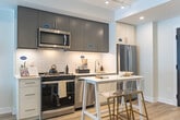Located at 41 Johnson Street in Barrie, Ontario, this thoughtfully designed one-bedroom, one-bathroom unit offers a compact yet functional layout across a single floor. The open-concept living and kitchen area is bright and airy, benefiting from large windows that allow generous natural light and provide views of the surrounding area. Light-toned hardwood-style flooring runs throughout, contributing to a clean, cohesive aesthetic.

The kitchen is a standout feature, equipped with a full suite of stainless steel appliances including a range, built-in microwave, dishwasher, and refrigerator. Two-toned cabinetry — white lower cabinets paired with taupe upper cabinets — frames a geometric white tile backsplash, adding a modern design element. A single-basin sink and light quartz countertops complete the practical yet stylish workspace.

The bedroom is a comfortable and quiet retreat, featuring sliding panel closet doors and the same warm flooring found throughout the unit. The bathroom is well-appointed with a white vanity, undermount sink, large mirror, and a full soaker tub with a curved shower rod and handheld shower fixture, finished in neutral tile. A dedicated in-suite laundry closet houses a stacked Whirlpool washer and dryer, adding everyday convenience to this well-designed space.